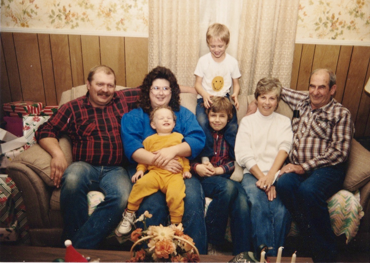 A photo of a family smiling and sitting together on a couch. It appears that the image was taken sometime in the 80s or 90s